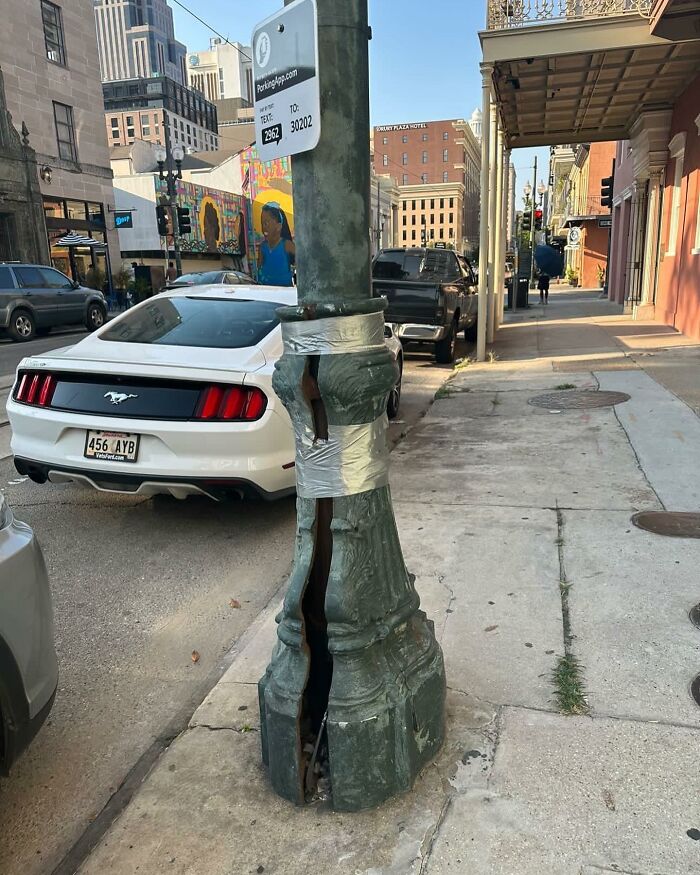 Damaged street lamp pole held together with duct tape on an urban sidewalk, showcasing weird street findings.