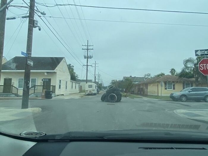View from inside a car showing a strange object made of tires blocking a residential street in an urban neighborhood.