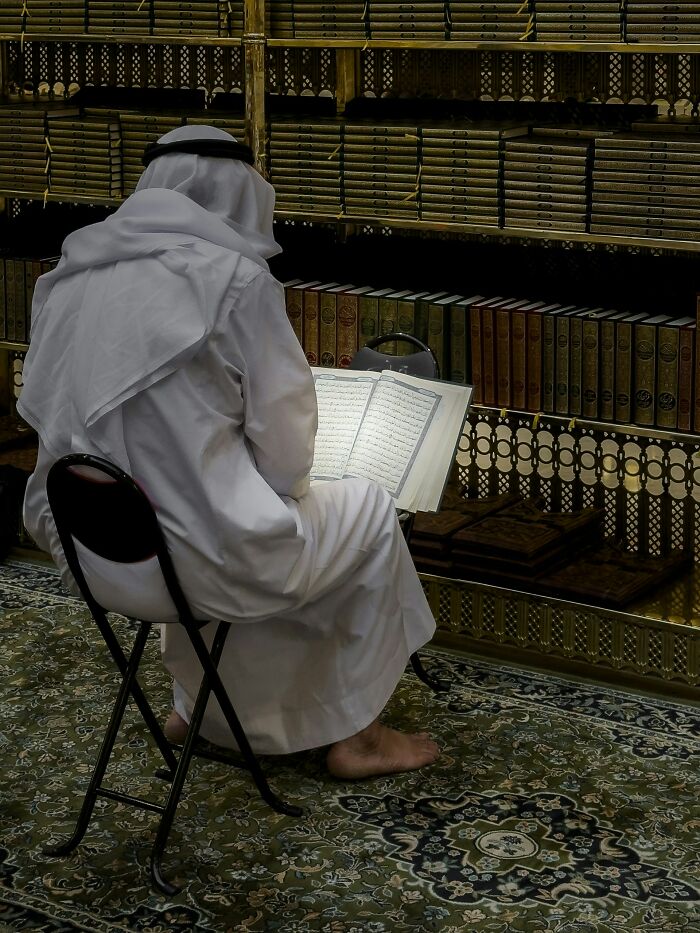 Man in traditional white attire reading a book in a room filled with shelves of books, depicting former cult members' reflection.