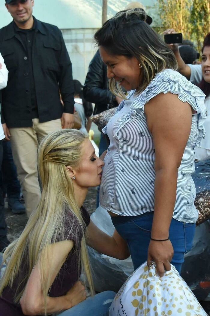 Blonde woman kissing a pregnant belly in a crowded outdoor setting, capturing a pop culture cringe moment.