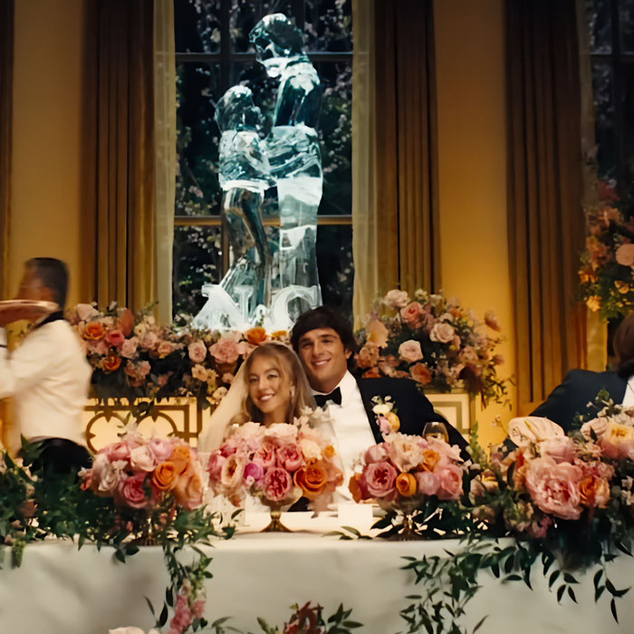 A wedding scene with Sydney Sweeney and a groom seated at a flower-filled table, part of Sydney Sweeney plays an adult star. A wedding scene with Sydney Sweeney and a groom seated at a flower-filled table, part of Sydney Sweeney plays an adult star.