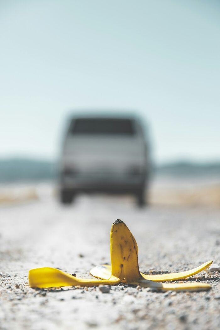 Banana peel on a dusty road with a blurred van in background, surreal scene evoking rained frogs