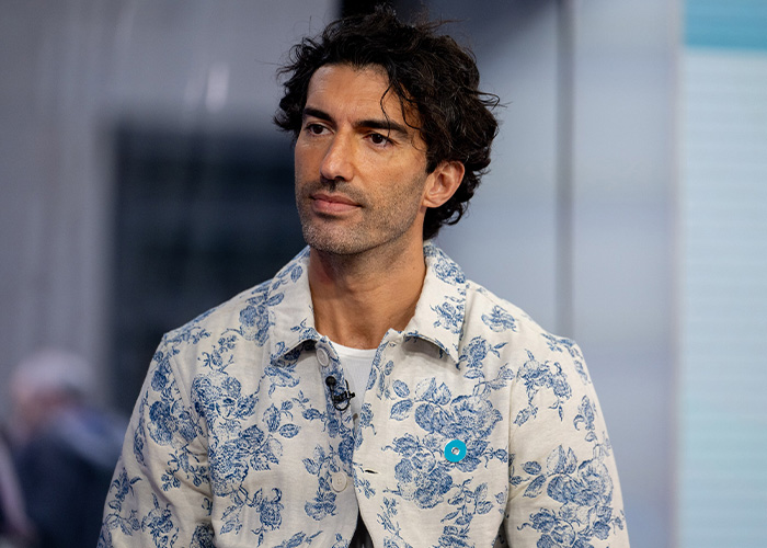 Man with curly dark hair wearing a white and blue floral shirt in a studio setting discussing British actress Jameela Jamil topics.