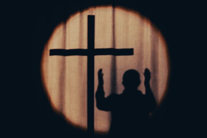 Shadow of a person raising hands near a cross symbol, representing former cult members reflecting on their experiences.