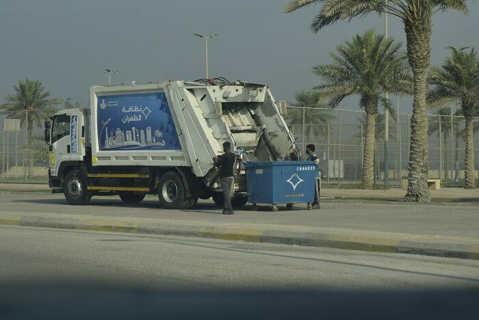 Two people working with a garbage truck collecting waste in a boring industry setting behind the scenes outdoors.