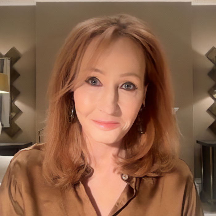 J.K. Rowling wearing a brown blouse, smiling softly in a warmly lit indoor setting with decorative mirrors in the background J.K. Rowling wearing a brown blouse, smiling softly in a warmly lit indoor setting with decorative mirrors in the background