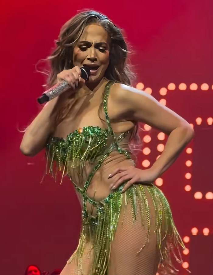 Jennifer Lopez performing on stage in a green fringe outfit, going viral after responding to dress her age comments.