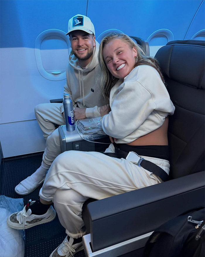 JoJo Siwa smiling in casual wear seated on an airplane, highlighting her dramatic transformation and name change.