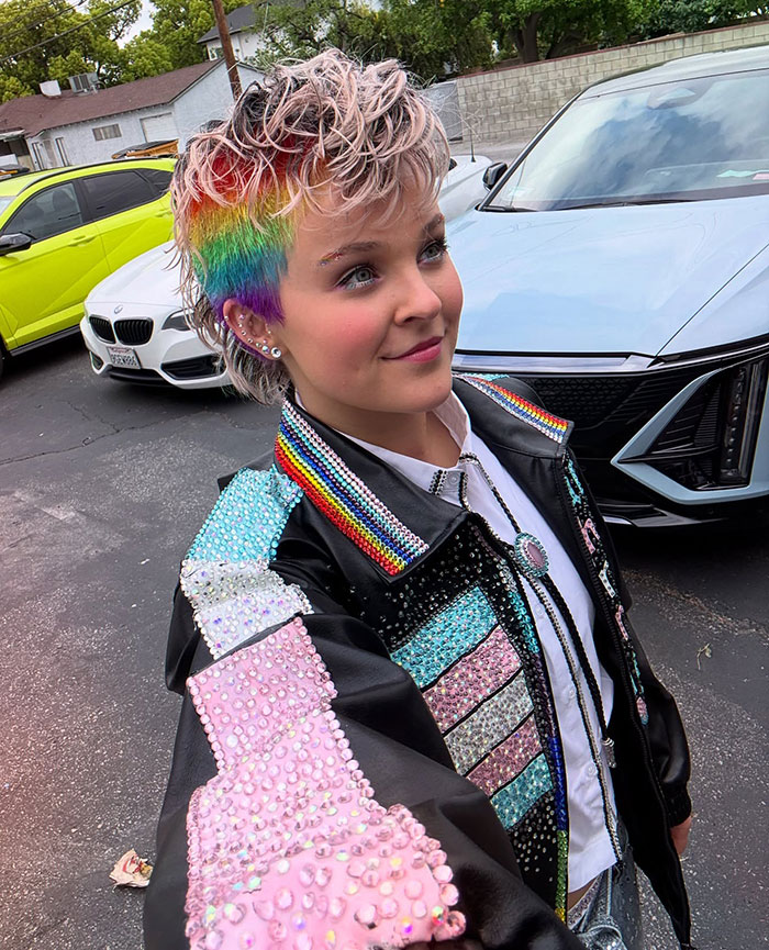JoJo Siwa with a rainbow hairstyle and colorful studded jacket showcasing her massive transformation and bold new look outdoors.