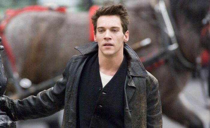 Young man in a worn leather jacket walking past horses, symbolizing celebs who went from rags to riches on their own.