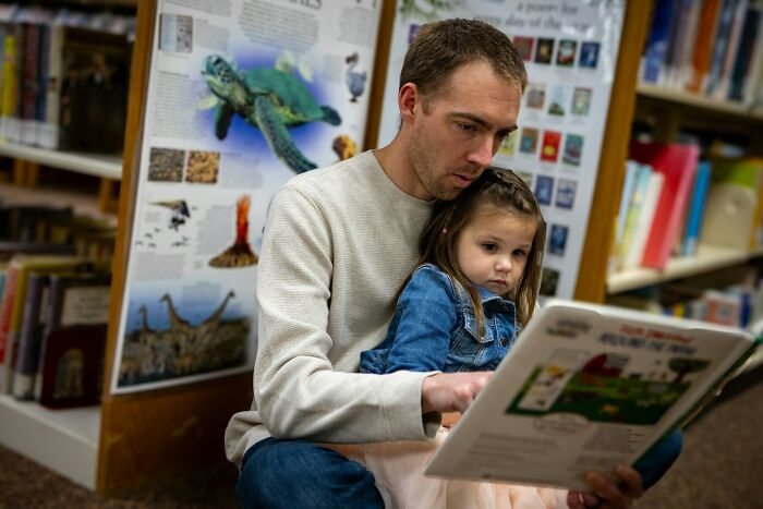 Man and young girl reading a book together in a library, capturing moments of surprised intelligence and learning.