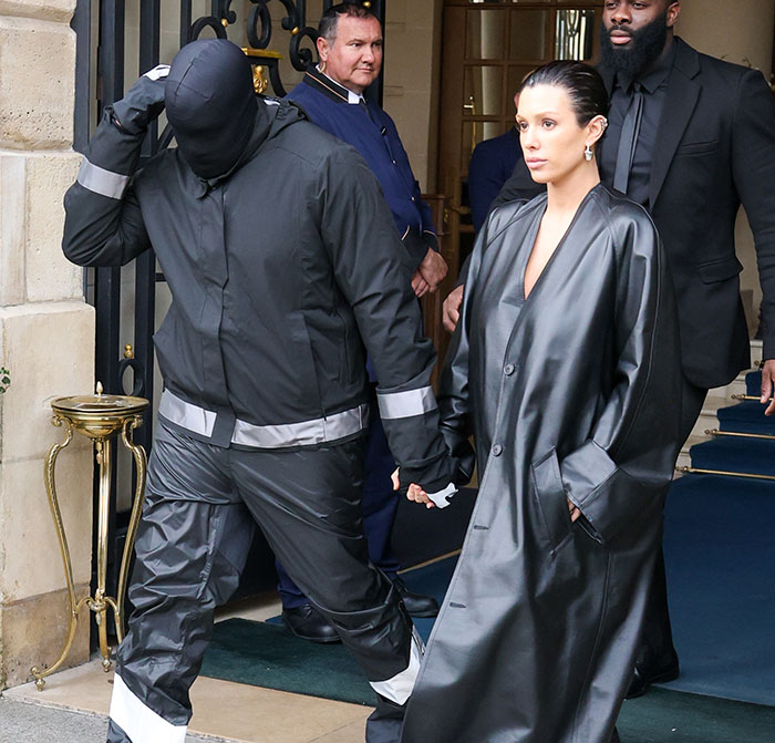 Kanye West in black outfit with hood, walking and holding hands, revealing health battle in public appearance.