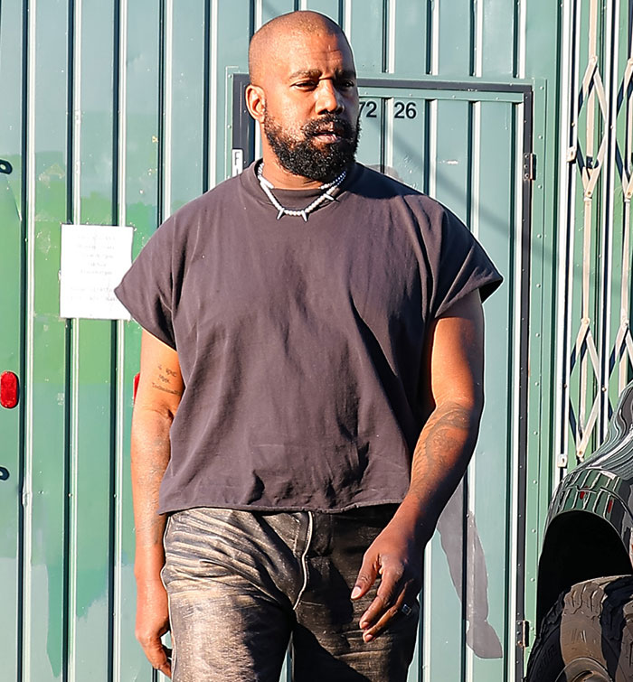 Kanye West walking outside wearing a black shirt and necklace, revealing his health battle in recent news coverage.