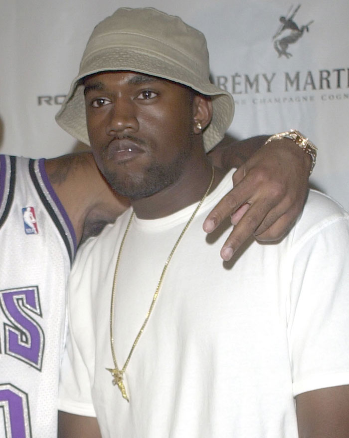 Kanye West wearing a beige bucket hat and white shirt, revealing health battle and issuing a deep apology.