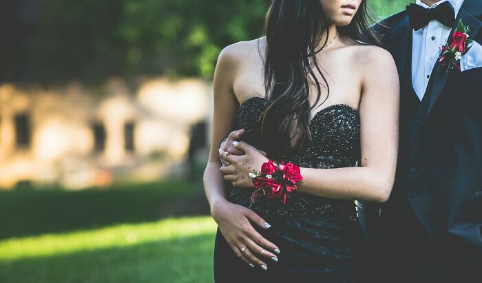 Young couple dressed for high school prom outdoors, showcasing elegant attire and corsage amid a casual setting.