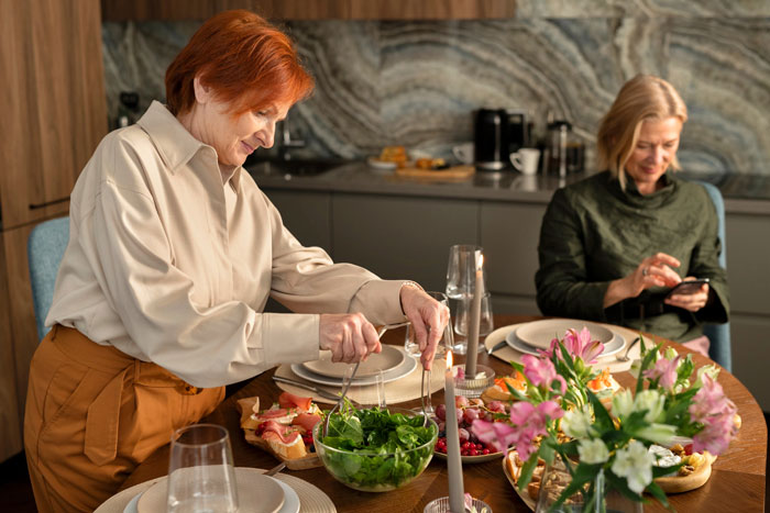 Two women at a dining table with food, illustrating family conflict involving a MIL and wedding planner controversy. Two women at a dining table with food, illustrating family conflict involving a MIL and wedding planner controversy.