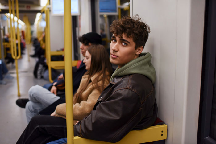 Teen on crowded metro looking annoyed as other riders deal with loud behavior on public transit.