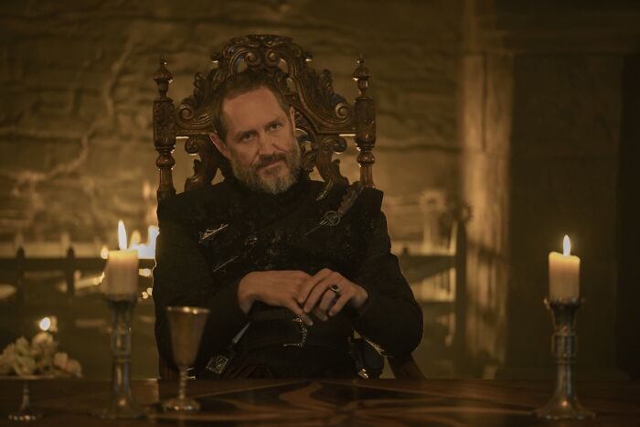 Actor portraying a Targaryen character seated on an ornate throne surrounded by candlelight in a medieval setting.