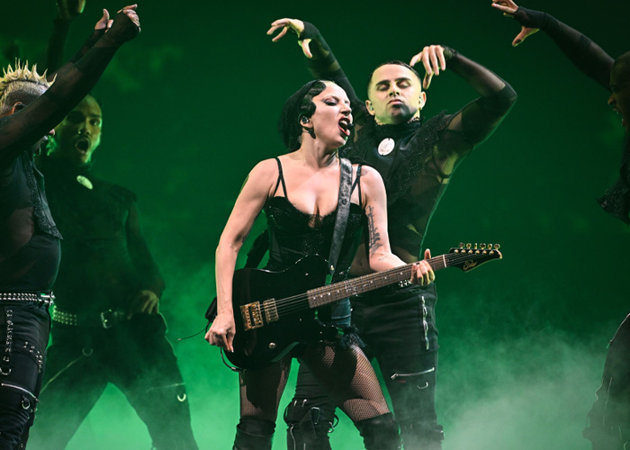 Lady Gaga performing on stage with guitar and dancers in dark outfits during bold ICE speech at her concert. Lady Gaga performing on stage with guitar and dancers in dark outfits during bold ICE speech at her concert.
