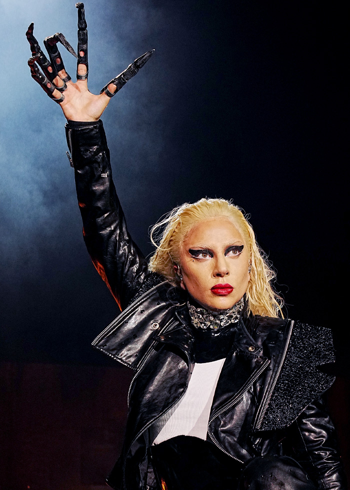 Lady Gaga in dramatic black outfit and glove raising hand during concert delivering bold ICE speech on stage. Lady Gaga in dramatic black outfit and glove raising hand during concert delivering bold ICE speech on stage.