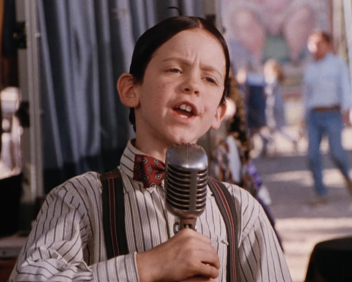 Child actor from Little Rascals speaking into a vintage microphone wearing a striped shirt and bow tie on set. Child actor from Little Rascals speaking into a vintage microphone wearing a striped shirt and bow tie on set.