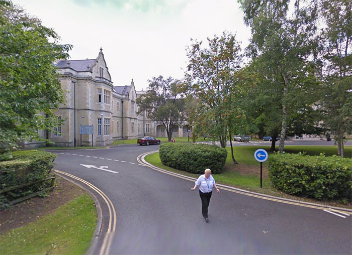 Person walking on a curved road near large building and trees, related to Barron Trump emergency call and operator interaction.
