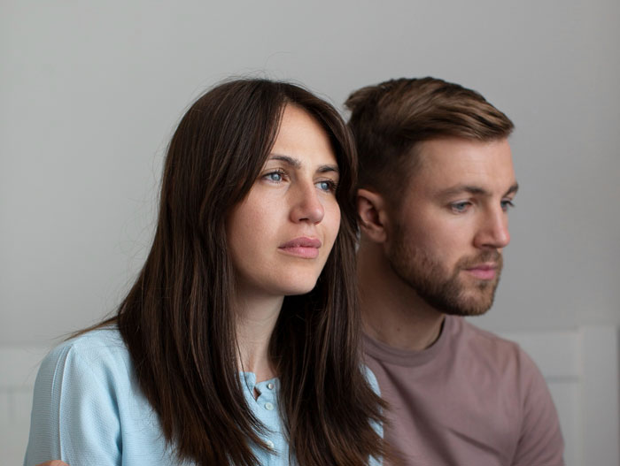 Couple sitting together looking serious and thoughtful, illustrating man jumps into hero mode for pregnant ex situation.