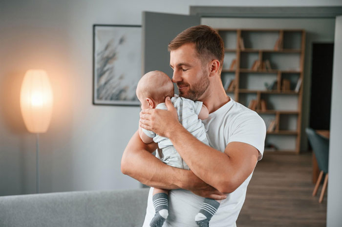 Man holding baby tenderly indoors, showing hero mode and commitment to raising child for pregnant ex.