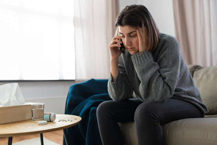 Pregnant woman sitting on couch, looking stressed while talking on phone, reflecting tension and emotional struggle.