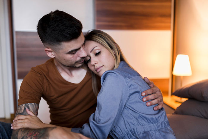 Man comforting pregnant ex in a bedroom, showing support and offering to raise her baby during difficult times.
