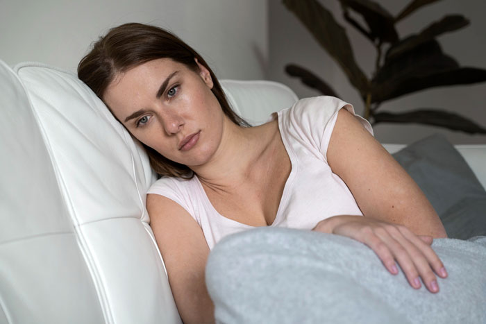 Young woman lying on a couch looking worried and contemplative, reflecting on relationship and pregnancy challenges