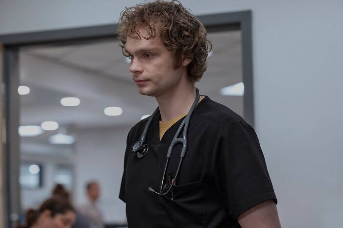 Young man in black scrubs with stethoscope in hospital hallway, representing new season 2 addition in Insufferable.