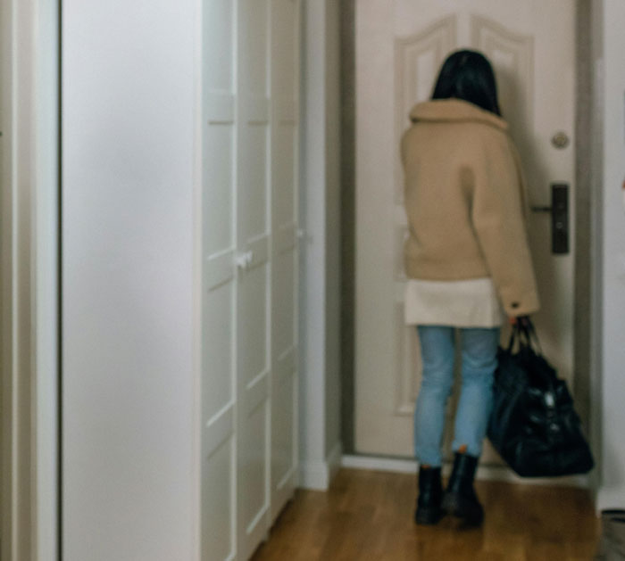 Teen woman standing alone by a closed door, holding a bag, conveying a plan to make him divorce her.