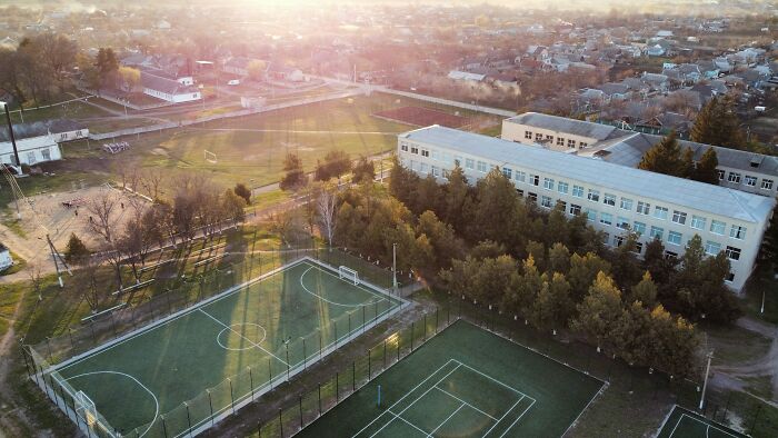 Aerial view of a high school campus at sunset with sports fields, trees, and surrounding neighborhood showing school controversies.