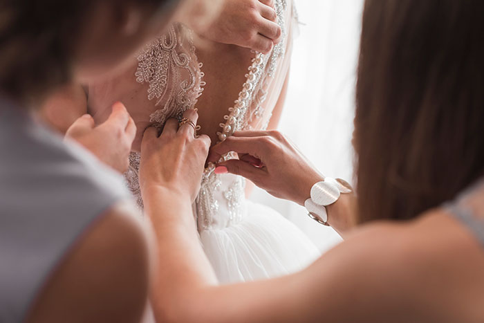 Hands adjusting a bride&rsquo;s dress, symbolizing a man considering canceling his wedding due to fianc&eacute;e&rsquo;s family hiring a PI.