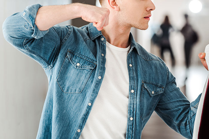 Young man in a denim shirt raises fist aggressively, representing anger and conflict related to family forgiveness and tension.