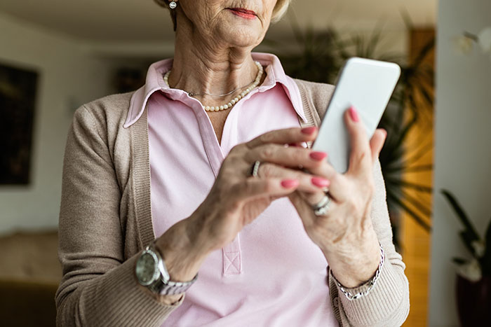 Older woman using smartphone, reflecting on family forgiveness and complex emotions over past conflict.
