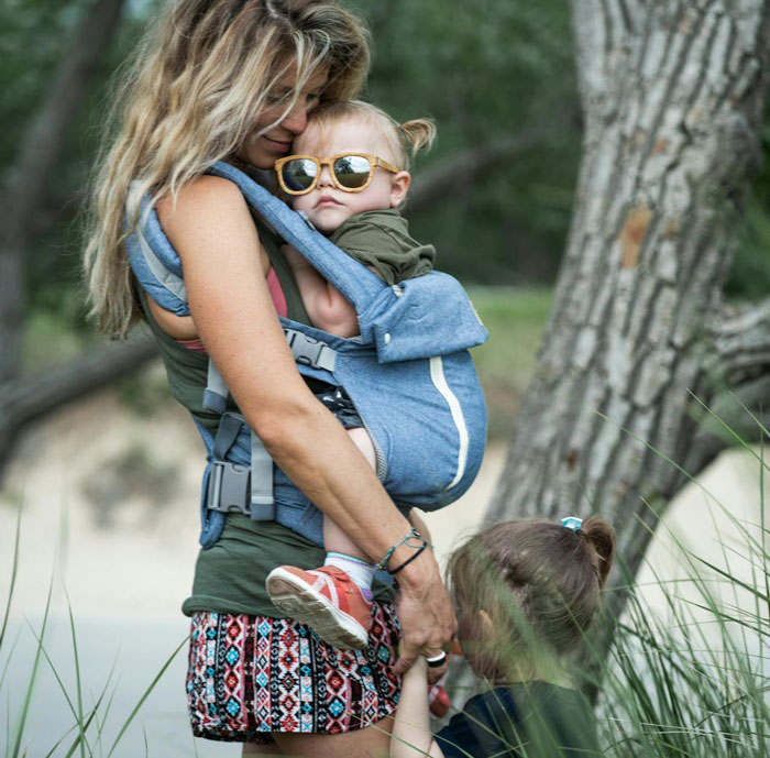 Mother carrying baby in a carrier outdoors while holding hands with another child, reflecting on dating challenges with kids. Mother carrying baby in a carrier outdoors while holding hands with another child, reflecting on dating challenges with kids.