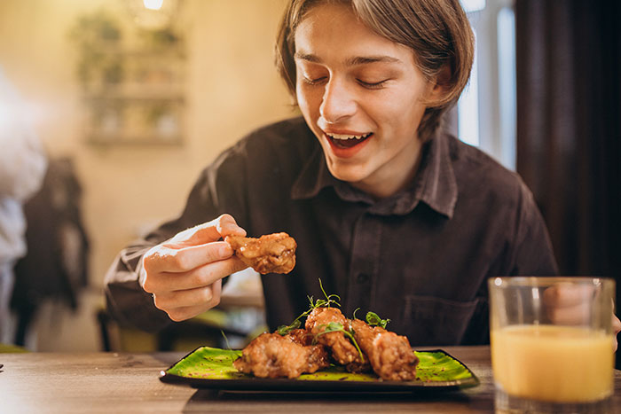 Young man enjoying crispy chicken wings at a restaurant, highlighting a unique dining experience and food innovation.