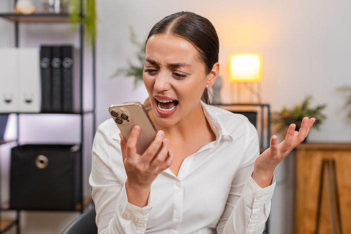 Angry woman looking at phone frustrated after dating disappointment, highlighting a lovey-dovey text and payment conflict.