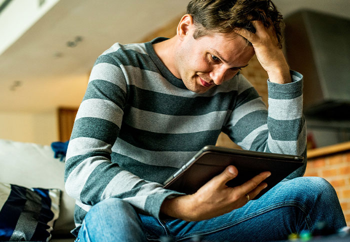 Man sitting in his apartment looking worried while holding a tablet, noticing strange things happening around him.