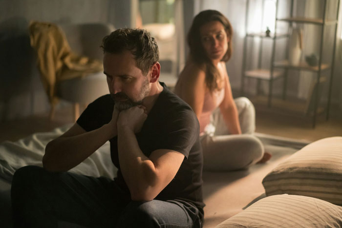 Man feeling guilty and distant from daughter during a messy divorce, woman sitting behind him appearing sad and distant.