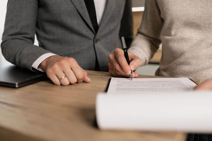 Man in suit and woman signing divorce papers at wooden table, capturing dad distancing from daughter during messy divorce.