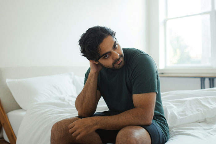 Man sitting on bed looking thoughtful, reflecting on a past relationship and princess syndrome years after breakup