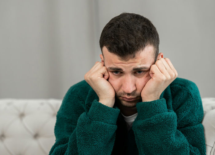 Man in green sweater sitting on couch looking pensive and regretful, reflecting on ex-girlfriend and princess syndrome.
