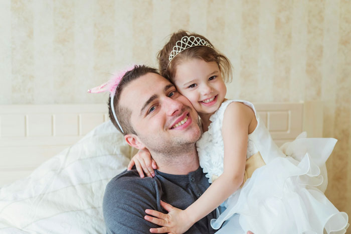 Man and young girl wearing princess tiaras, smiling and showing affectionate moment, highlighting princess syndrome concept.