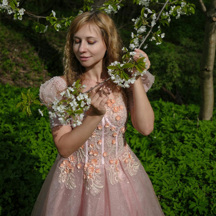 Woman in a pink princess dress holding blooming branches, evoking princess syndrome in a natural outdoor setting
