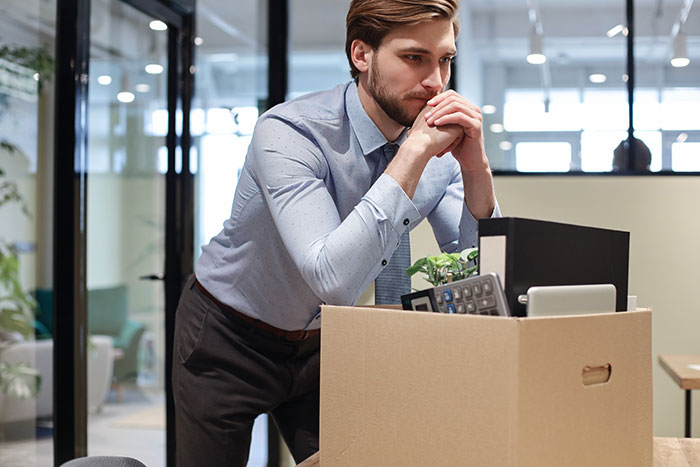 Man with packed box in office appearing thoughtful, symbolizing revenge on coworker who got him fired years ago.