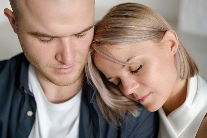 Couple leaning on each other looking down, depicting emotional distress after a hospital incident and family mistreatment. Couple leaning on each other looking down, depicting emotional distress after a hospital incident and family mistreatment.