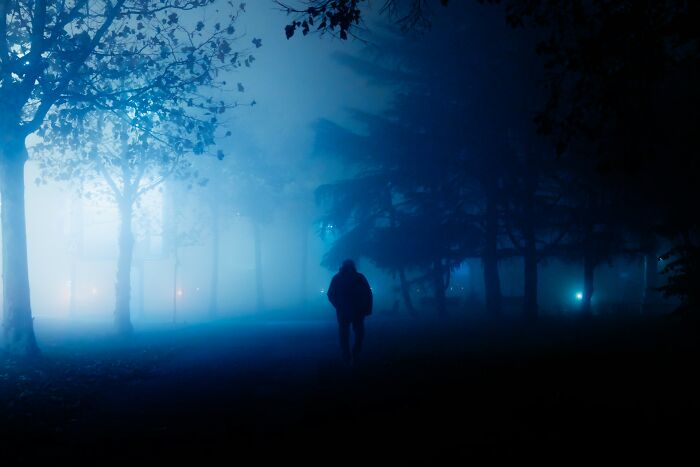 Silhouette of a lone woman walking through a foggy, dark park at night, illustrating feeling safer while living alone.